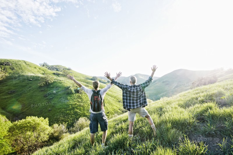 Caucasian father and son cheering on grassy hillside
