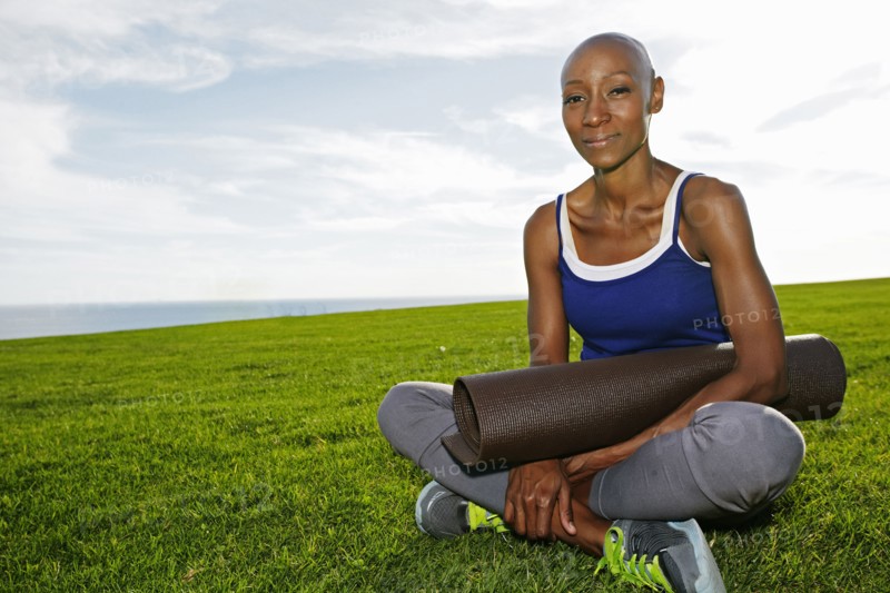 African American woman holding yoga mat in park