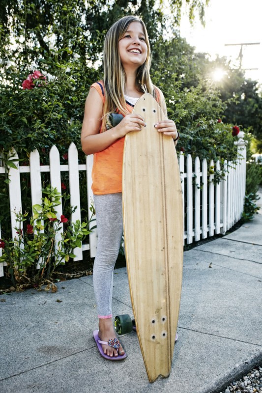 Caucasian girl holding skateboard on sidewalk