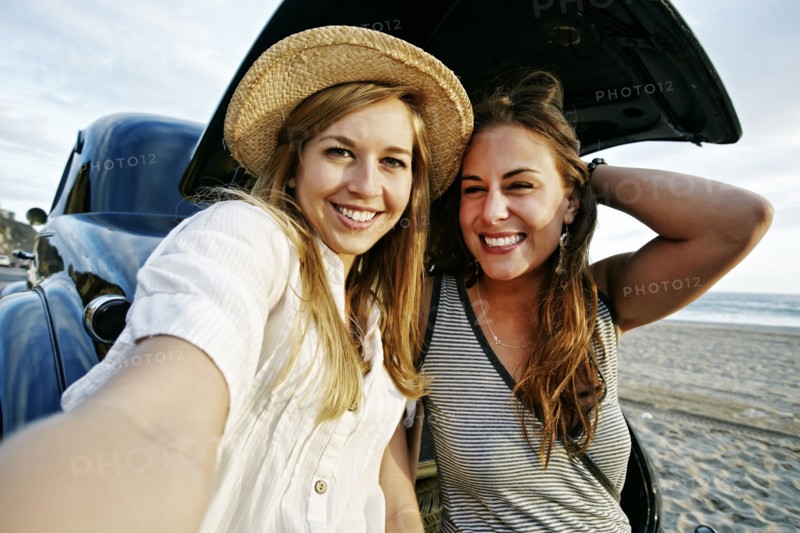 Women taking selfie in vintage car on beach