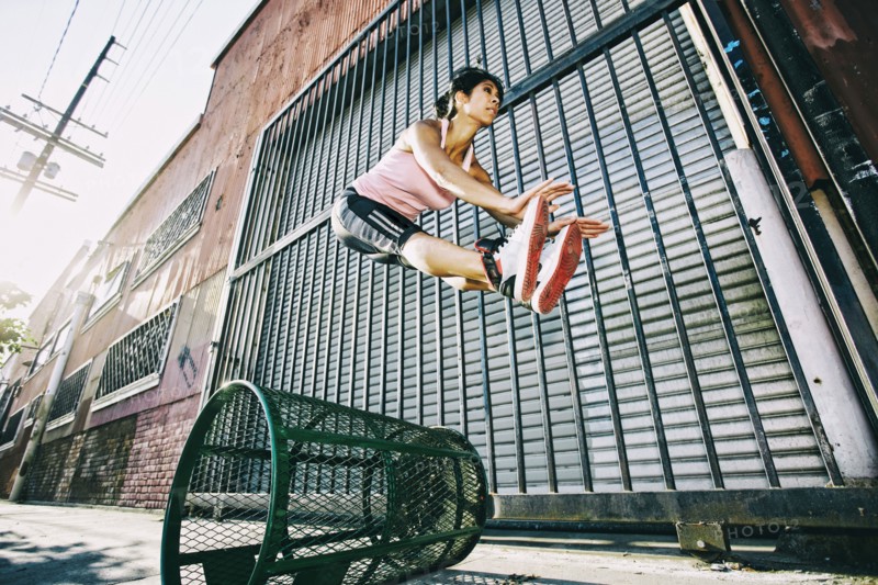 Mixed race woman jumping over trash can