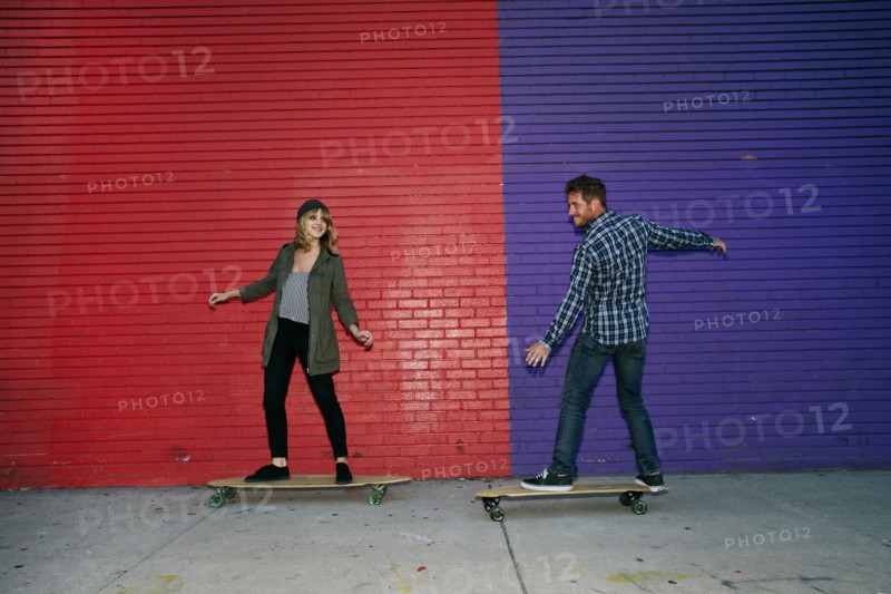 Caucasian couple riding skateboards on sidewalk