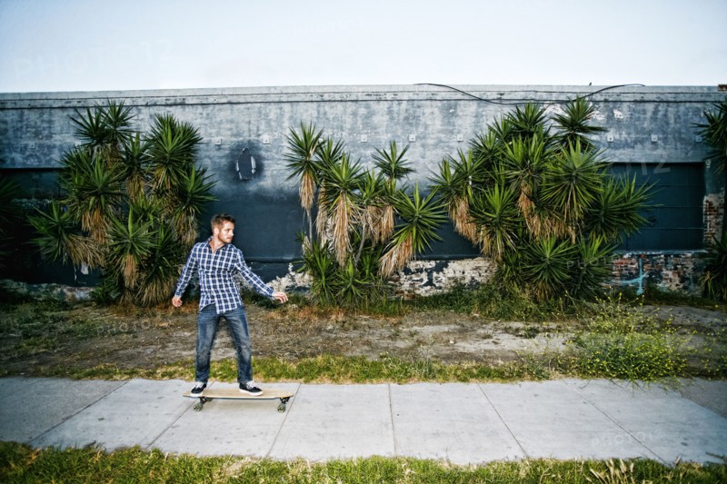 Caucasian man riding skateboard on sidewalk