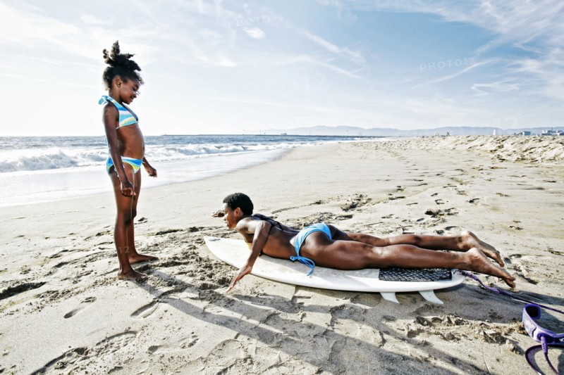 Black mother teaching daughter to surf on beach