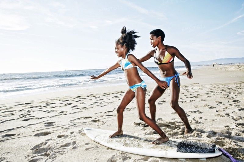 Black mother teaching daughter to surf on beach