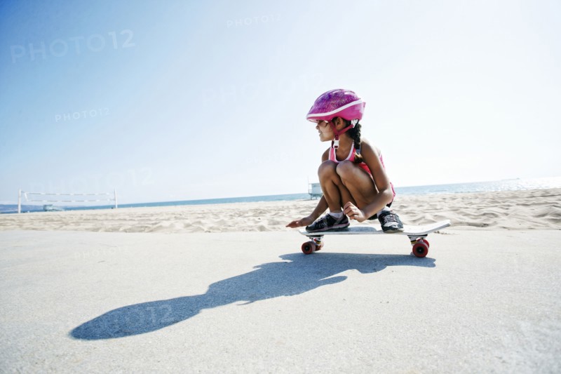 Mixed race girl riding skateboard at beach