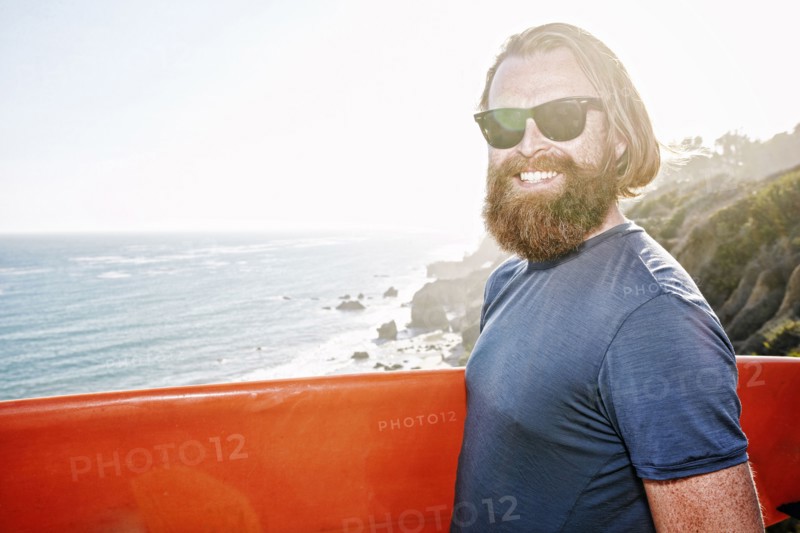 Caucasian man holding surfboard on coastal cliff
