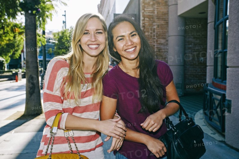 Women walking arm-in-arm on sidewalk