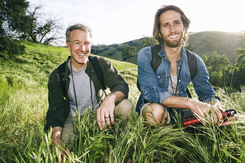 Caucasian hikers crouching in grass on mountain