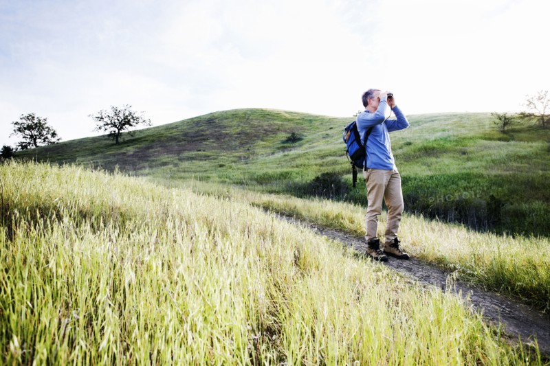 Caucasian man using binoculars on dirt path