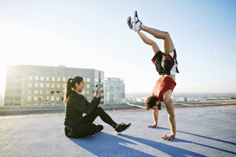 Woman photographing man doing handstand on urban rooftop