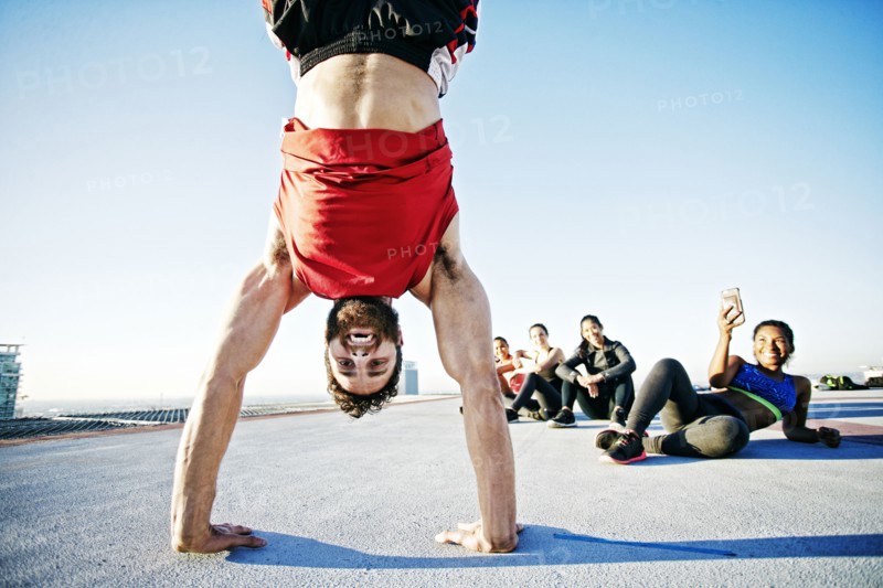 Woman photographing man doing handstand on urban rooftop