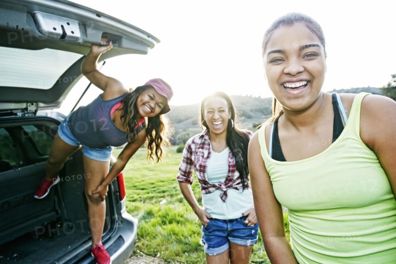 Mixed Race mother and daughters at hatch of car laughing