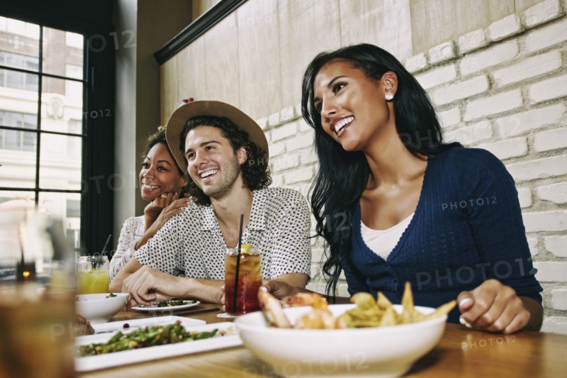 Smiling friends enjoying food and cocktails at table in bar