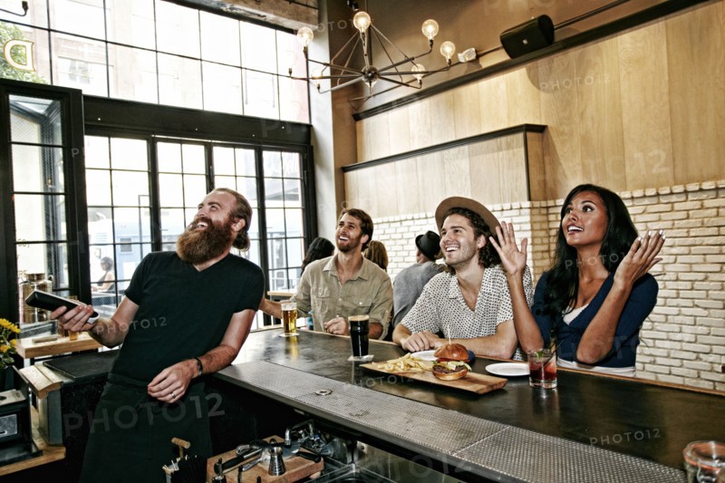 Smiling bartender and customers watching television in bar