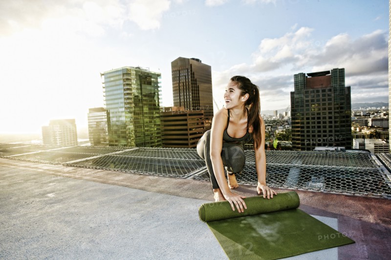 Caucasian woman rolling exercise mat on urban rooftop after yoga
