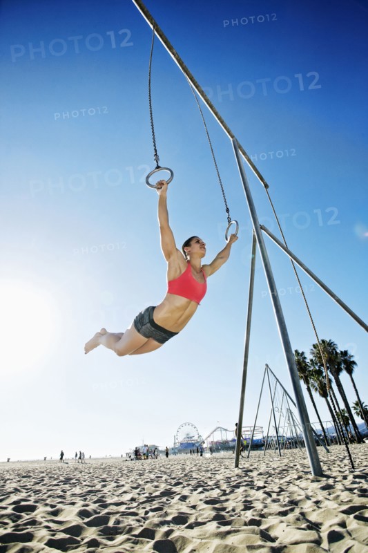 Caucasian woman using gymnastic rings at beach