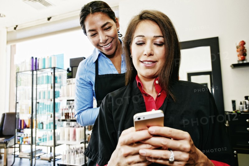 Hairdresser watching customer texting on cell phone in hair salon