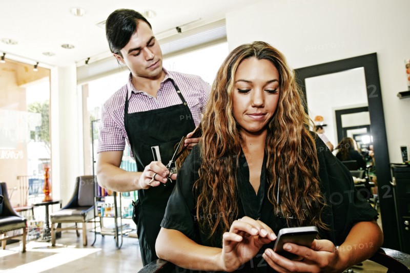 Hairdresser with customer texting on cell phone in hair salon