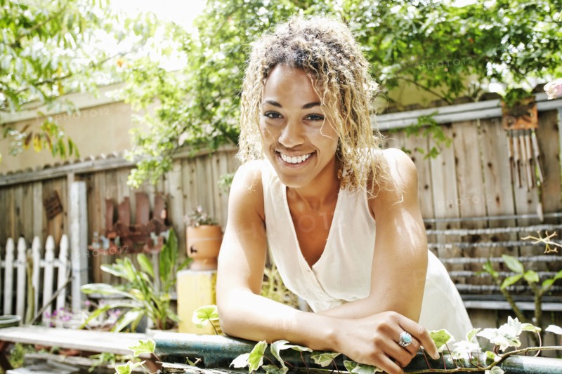 Smiling Mixed Race woman leaning on fence in garden