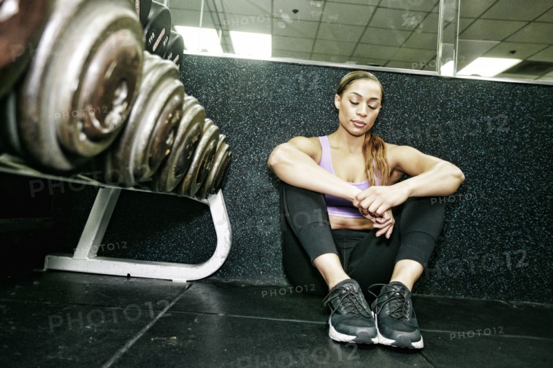 Mixed Race woman sitting on floor resting in gymnasium