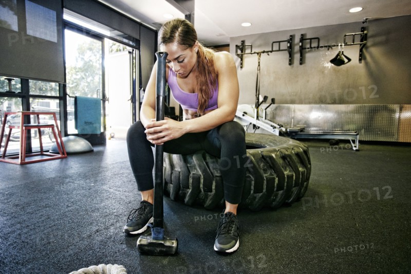 Mixed Race woman resting on tire holding sledgehammer in gymnasium