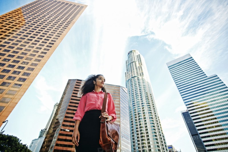 Serious Hispanic businesswoman near highrises in city