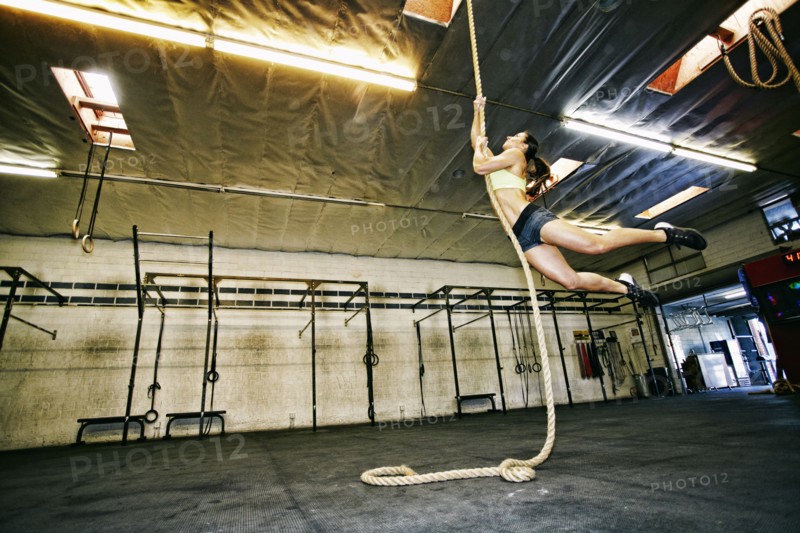 Mixed Race woman climbing rope in gymnasium