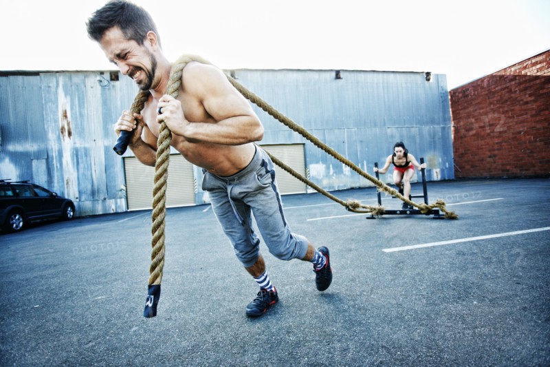 Caucasian man pulling woman with heavy ropes in parking lot outdoors