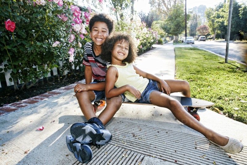 Mixed Race brother and sister sitting on skateboard on sidewalk