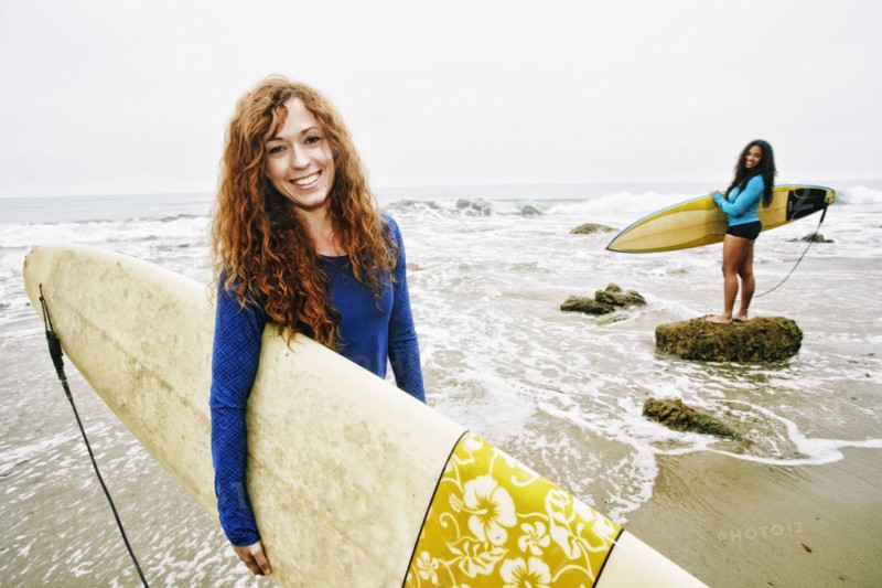 Smiling women holding surfboards at beach
