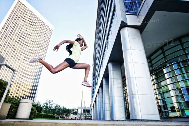 Black woman running and jumping on city sidewalk