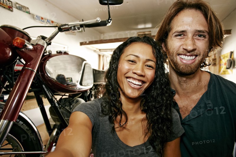 Man and woman posing for selfie with motorcycle in garage