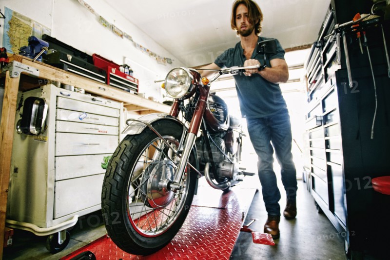 Caucasian man pushing motorcycle on repair stand in garage