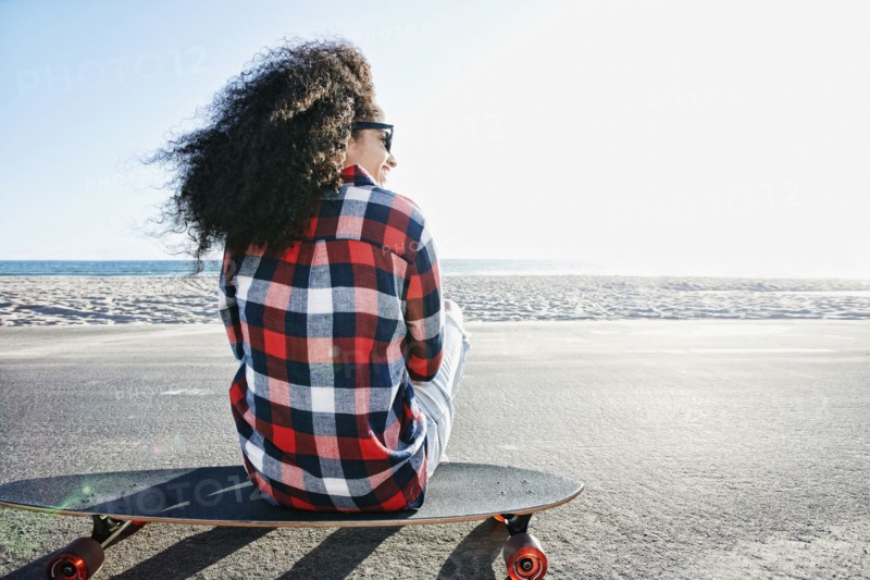 Hispanic woman sitting on skateboard at beach