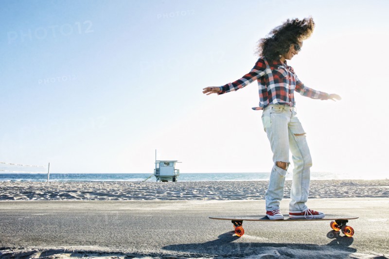 Hispanic woman riding skateboard at beach