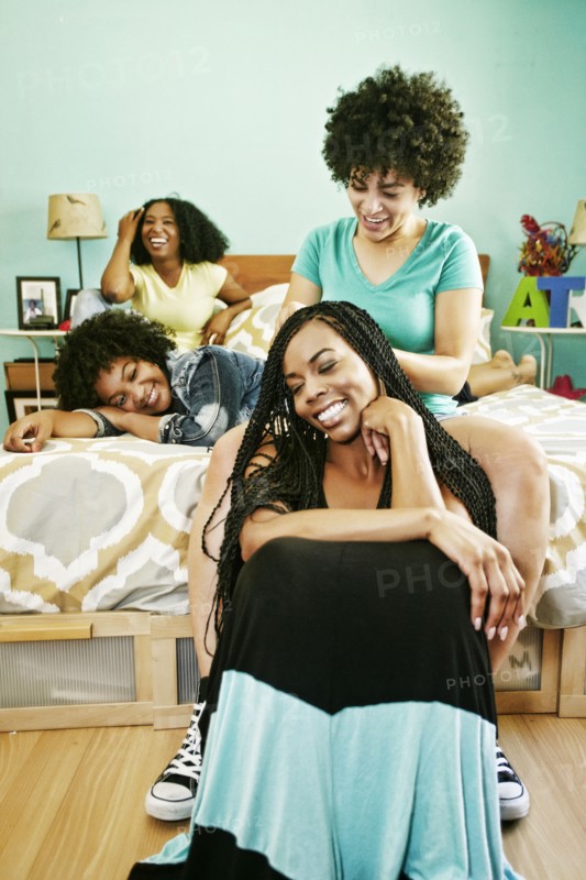 Woman braiding hair of friend in bedroom