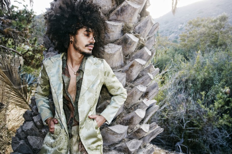 Mixed Race man wearing jacket leaning on tree trunk