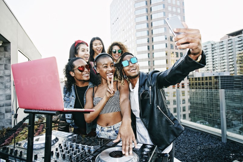 Friends posing for cell phone selfie with DJ on urban rooftop