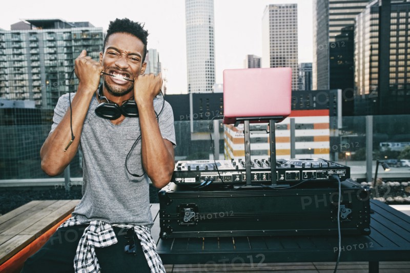 Black DJ biting headphones cord on urban rooftop