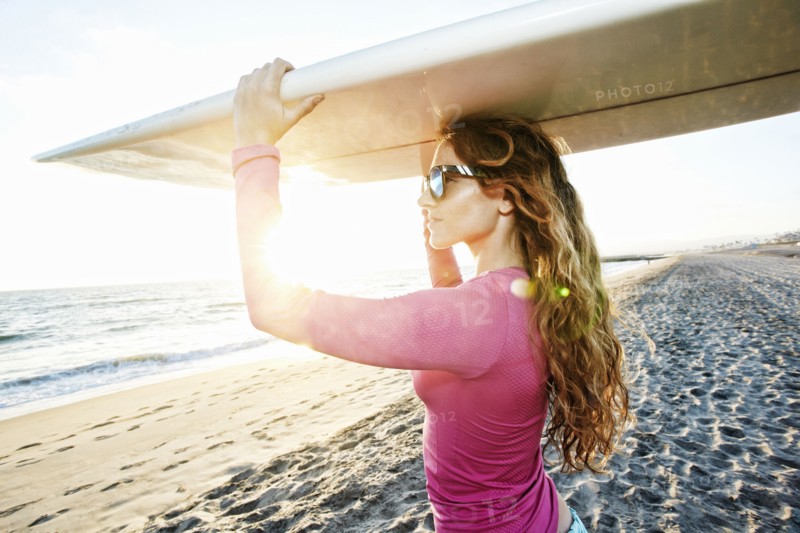 Caucasian woman carrying surfboard on beach