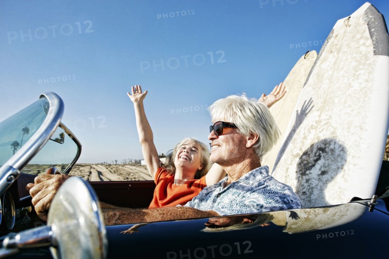 Older Caucasian couple in convertible car with surfboards on beach
