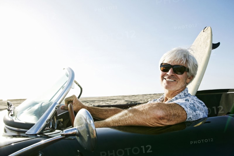 Older Caucasian man in convertible car with surfboard on beach