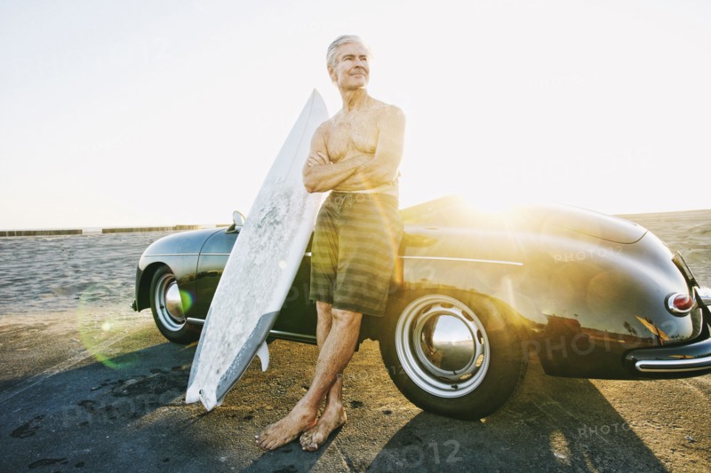 Older Caucasian man on leaning on convertible car with surfboard