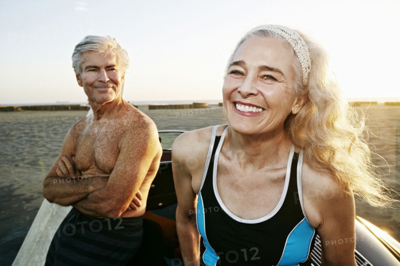 Older Caucasian couple leaning on convertible car at beach