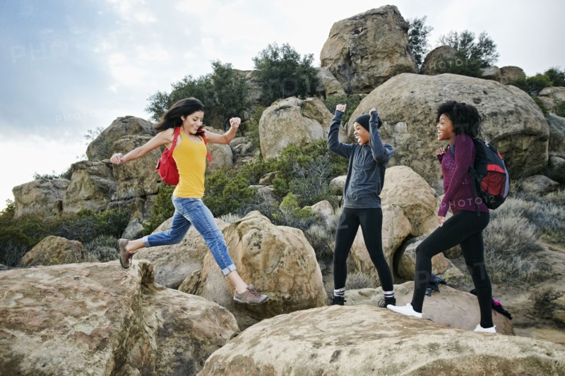 Women cheering friend jumping on rock formation
