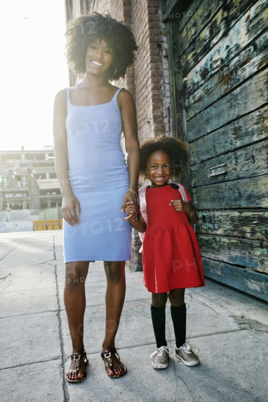 Portrait of smiling mother and daughter standing on sidewalk