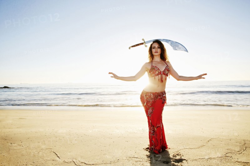 Caucasian belly dancer on beach balancing sword on head