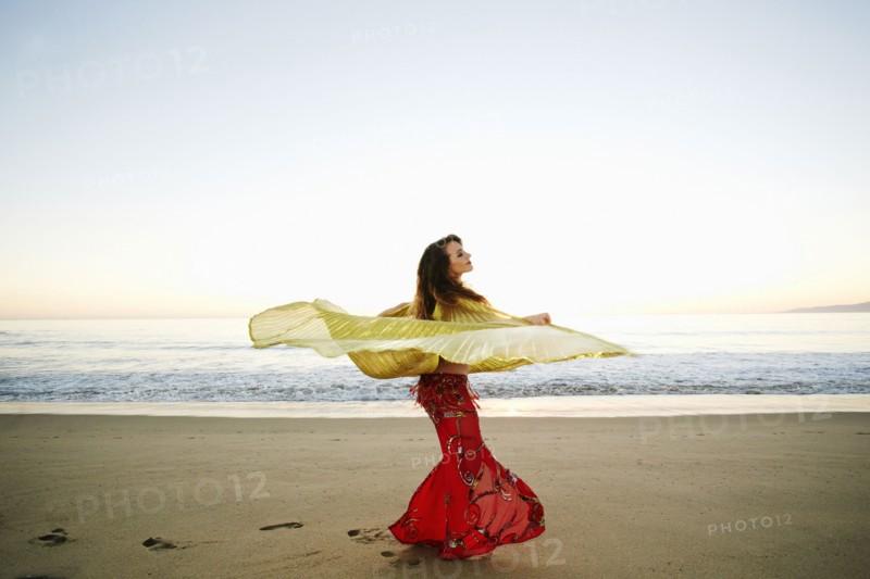 Caucasian belly dancer twirling cape on beach