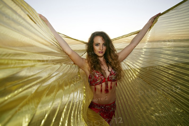 Caucasian belly dancer holding cape on beach
